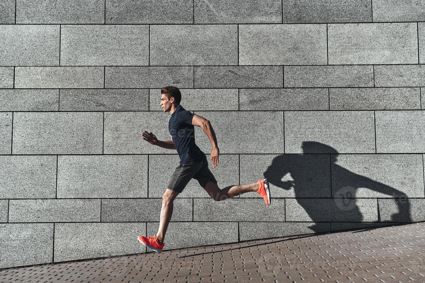 Healthy habits. Full length of young man in sports clothing running while exercising outside photo