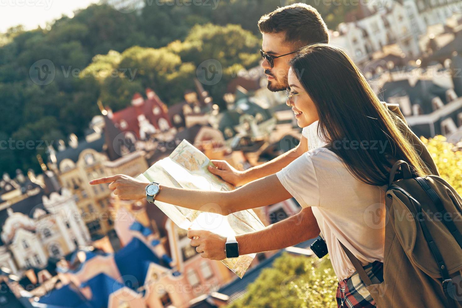 Curious young couple of tourists examining map and smiling while standing outdoors photo