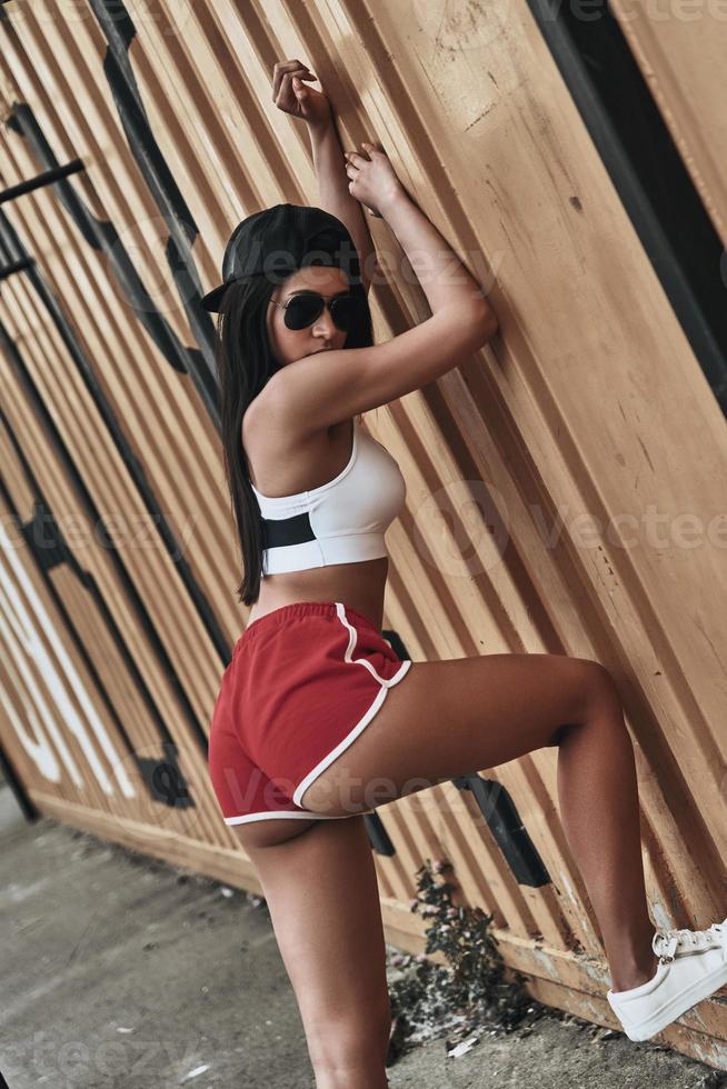 Showing off her best curves. Beautiful young woman in sports uniform looking at camera while standing outdoors photo
