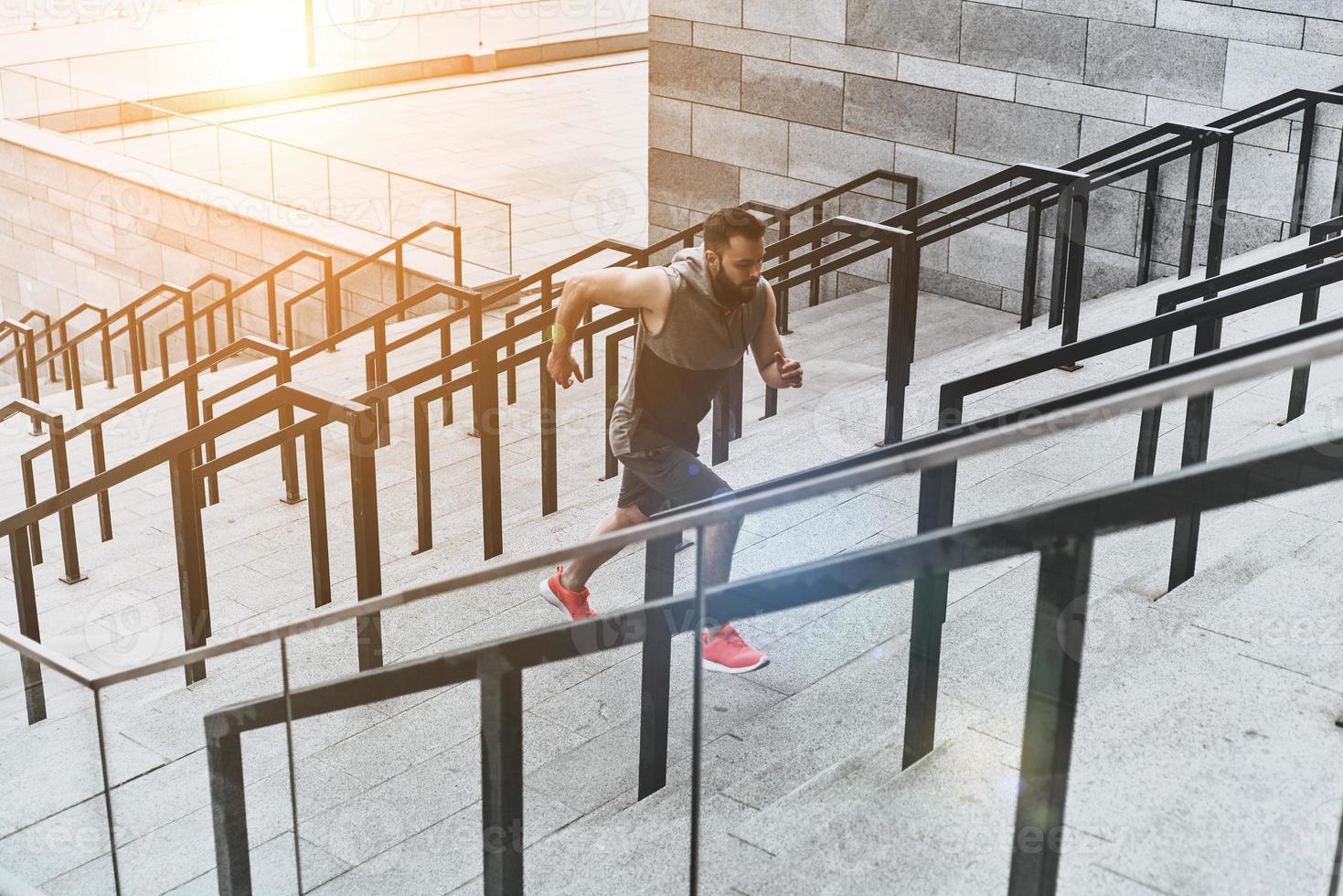 Giving all his best to achieve success. Full length of young man in sport clothing running up the stairs while exercising outside photo
