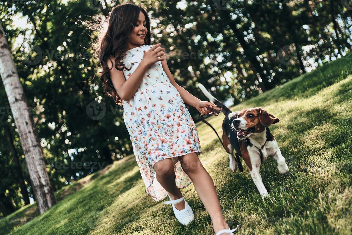 Friends forever. Full length of cute little girl playing with her dog and smiling while running outdoors photo