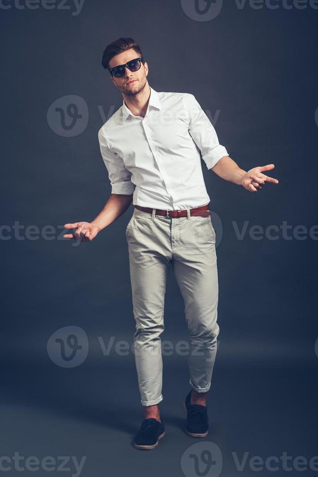 Who is your daddy Full length of confident young handsome man in sunglasses gesturing and looking at camera while standing against grey background photo