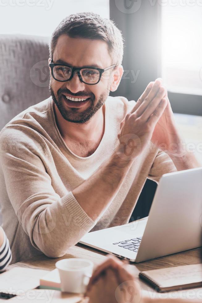Satisfied with his work. Close-up part of handsome young man discussing something with his coworkers with smile while sitting at the office table photo