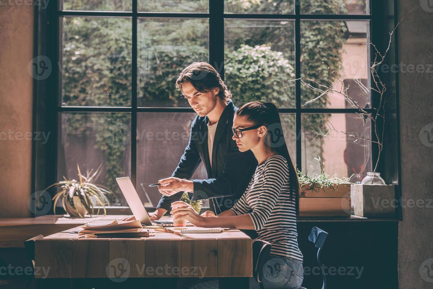 She needs an expert advice. Confident young man and woman working together while sitting at the wooden desk in creative office or cafe photo