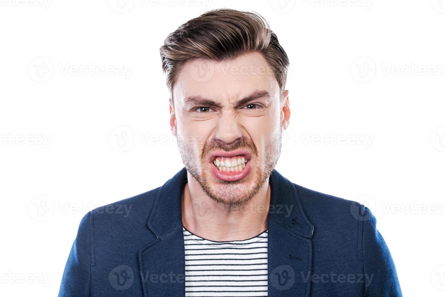 Furious man. Portrait of furious young man grimacing and looking at camera while standing against white background photo