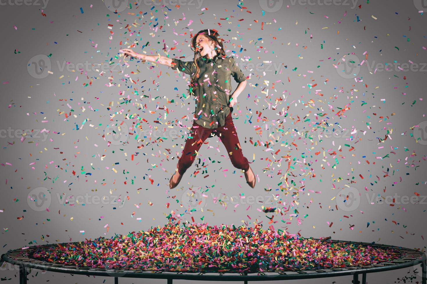 Fun in motion. Mid-air shot of beautiful young woman jumping on trampoline with confetti all around her photo