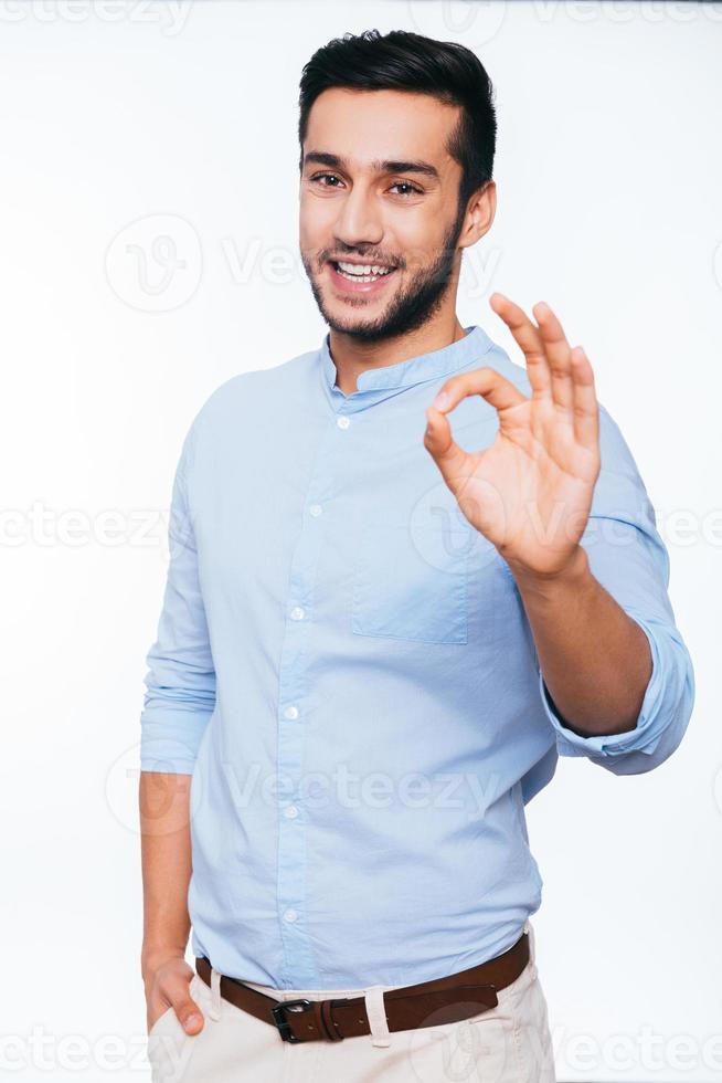 Everything is OK Confident young Indian man gesturing OK sign and smiling while standing against white background photo