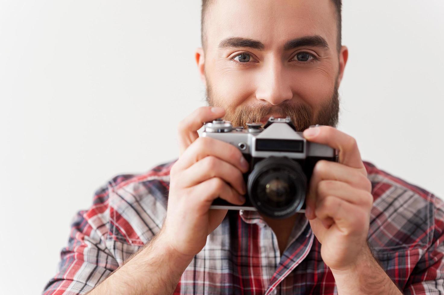 centrándose en ti. hombre joven con barba enfocándose en ti con su cámara retro mientras está de pie contra el fondo gris foto