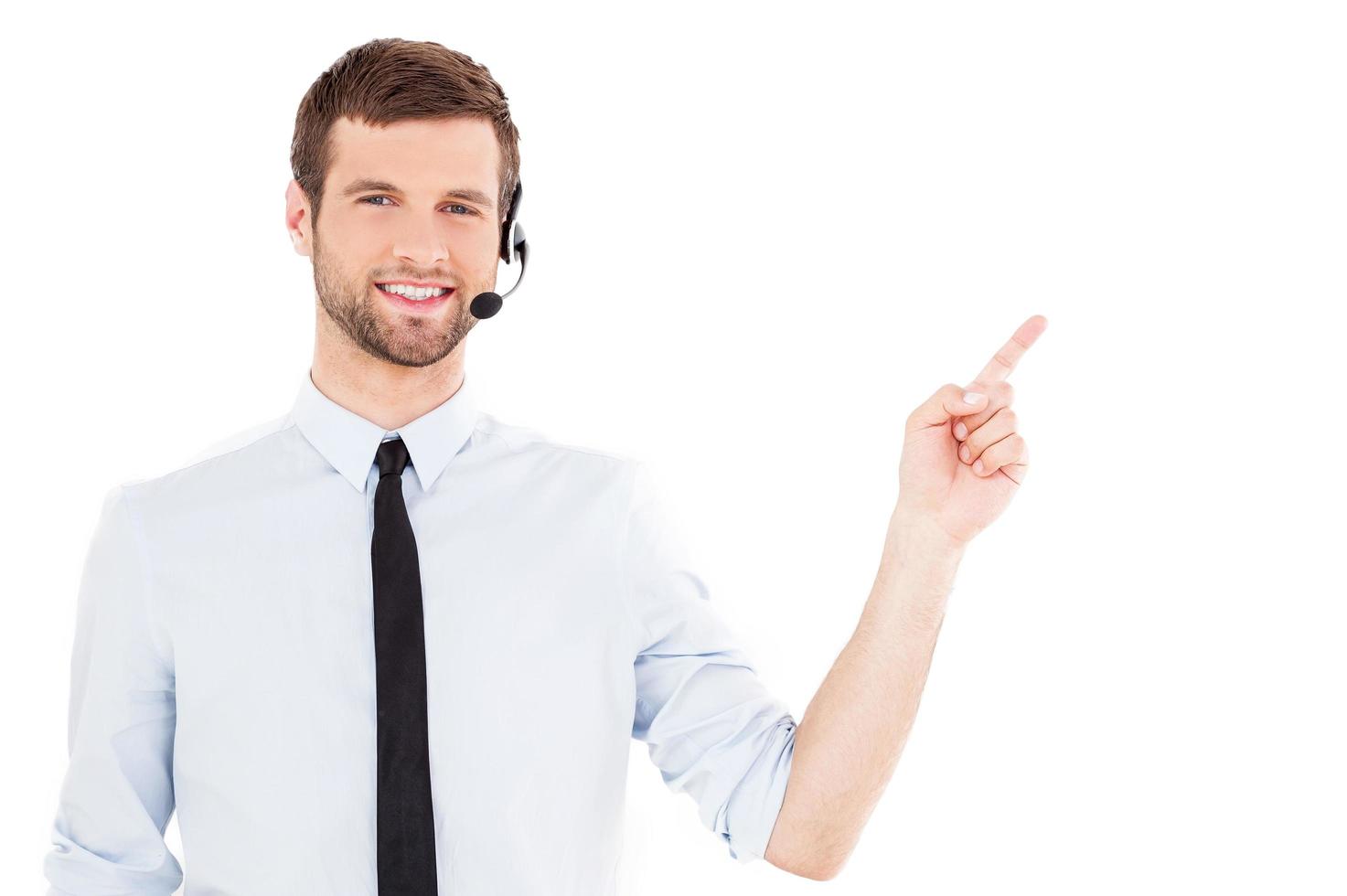 Operator pointing copy space. Handsome young man in formalwear and headset looking at camera and pointing away while standing isolated on white background photo