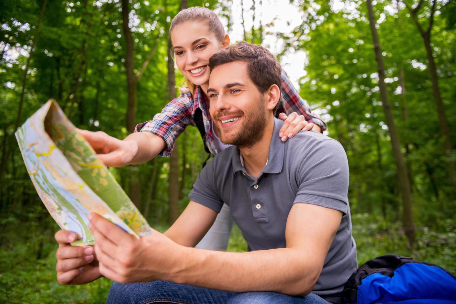 Tourists examining map. Thoughtful young couple with backpacks examining map while standing in nature photo