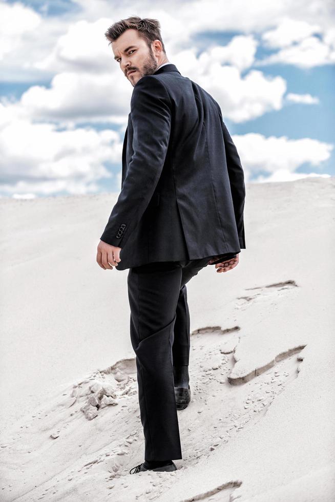 He is on his way to success. Rear view of young man in formalwear rising up by desert dune photo