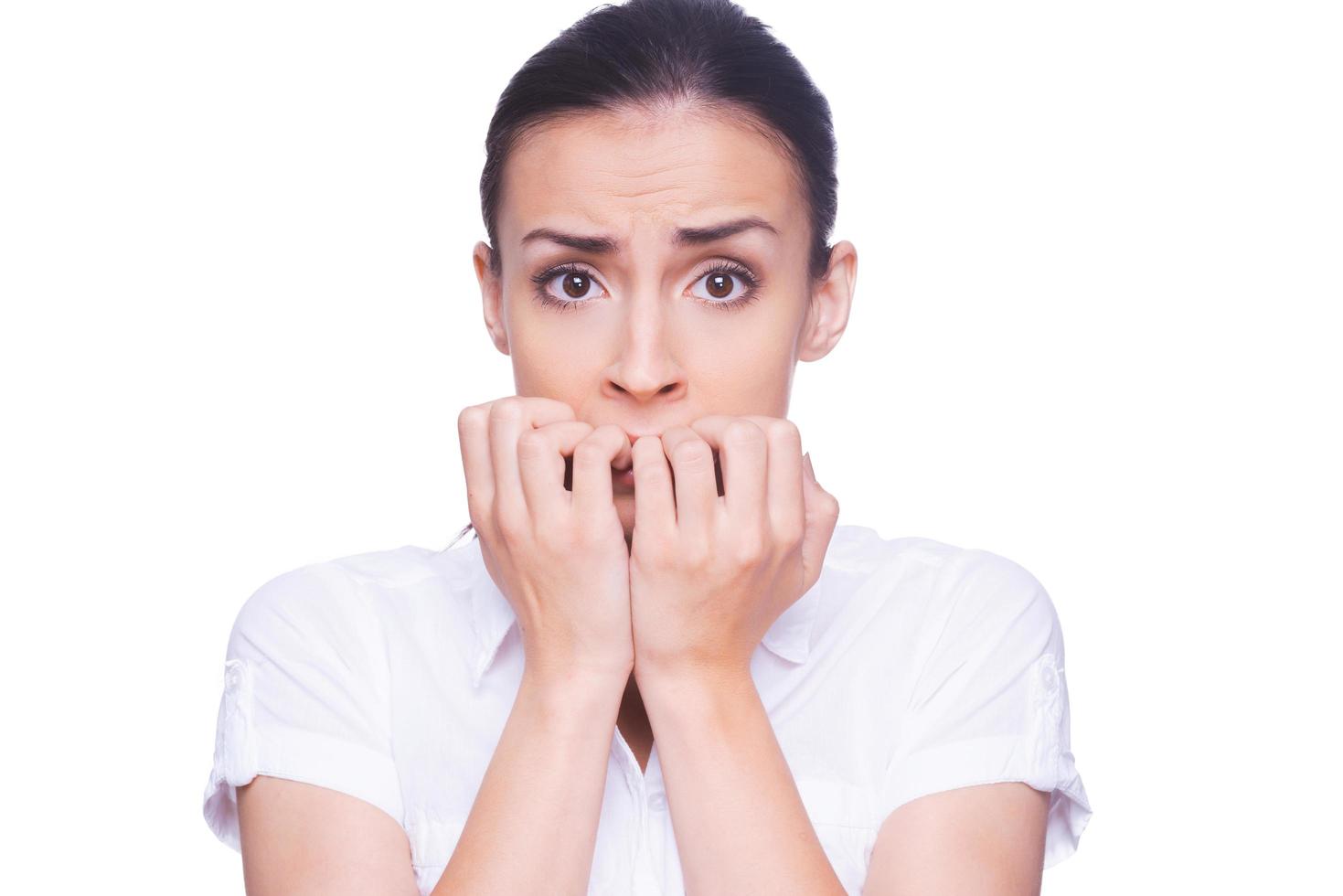 Terrified woman. Terrified young woman in formalwear looking at camera and biting nails while standing isolated on white photo