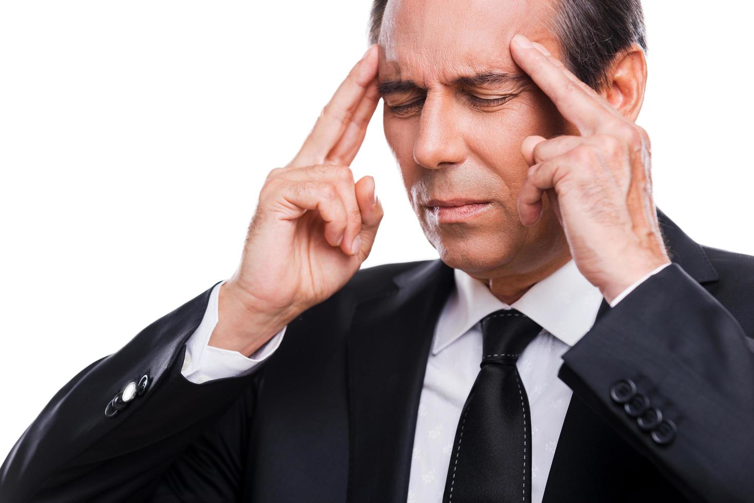 He got stressful job. Frustrated mature man in formalwear touching head with fingers and keeping eyes closed while standing against grey background photo