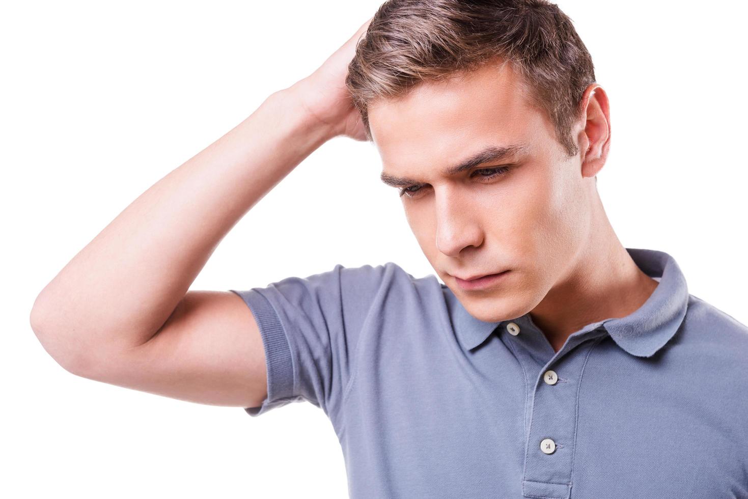 Failed again. Depressed young man holding hand in hair and looking down while standing isolated on white background photo