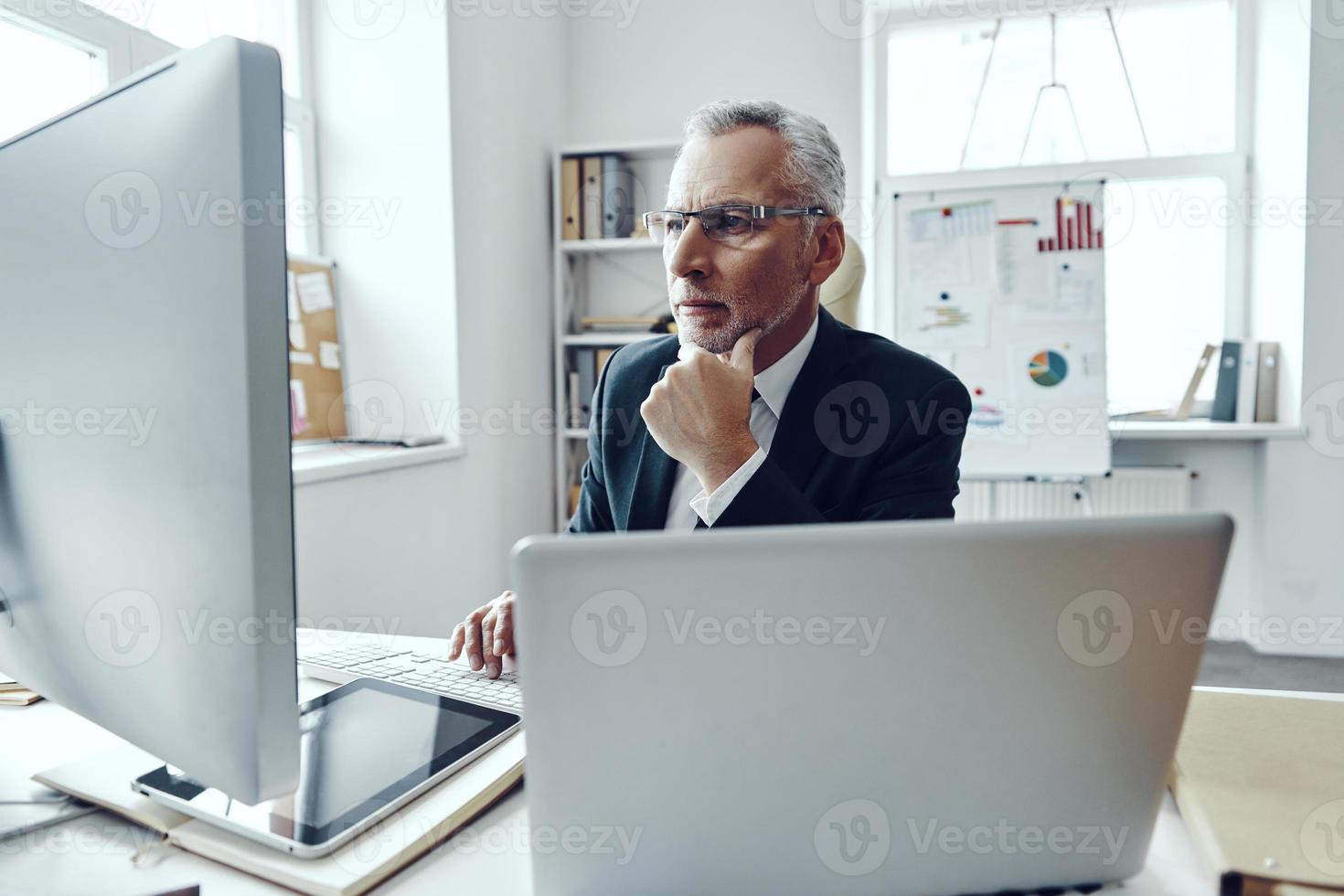 Senior man in elegant business suit using modern technologies while working in modern office photo