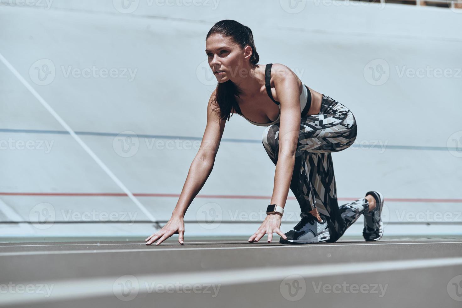 Ready to run. Beautiful young woman in sports clothing standing on the start line while running outdoors photo