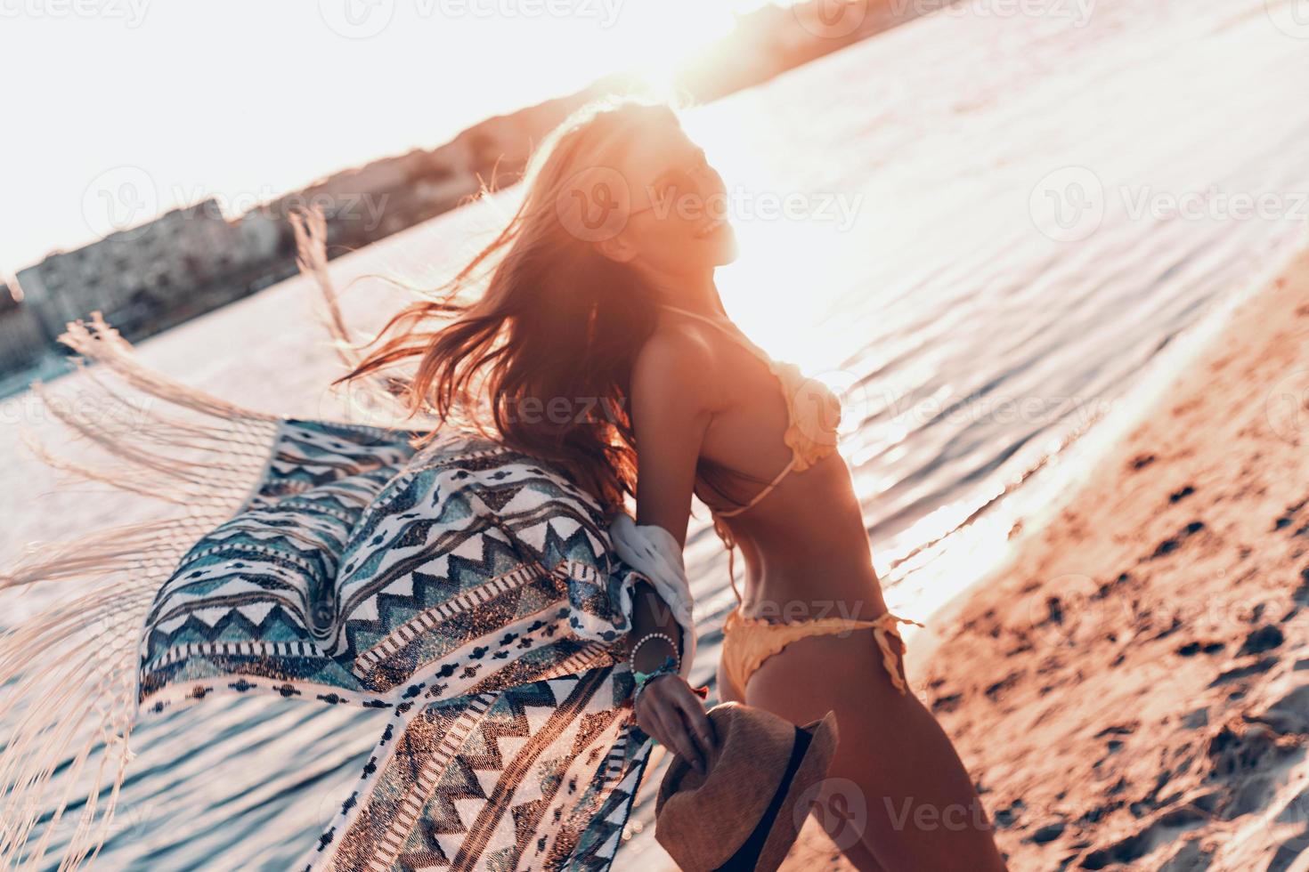 belleza despreocupada. atractiva mujer joven sonriendo mientras está de pie en la playa al aire libre foto