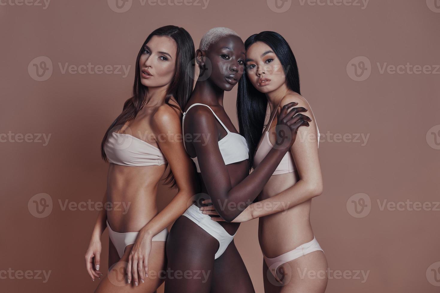 Looking perfect. Three attractive mixed race women looking at camera while standing against brown background photo