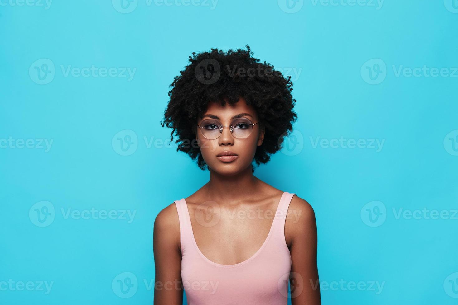 Charming girl. Attractive young African woman looking at camera while standing against blue background photo