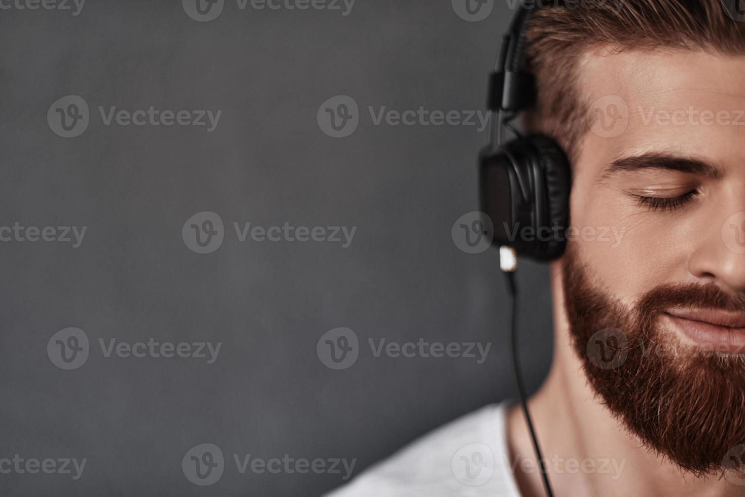 Listening with his heart.  Close up of good looking young man half face listening music while standing against grey background photo