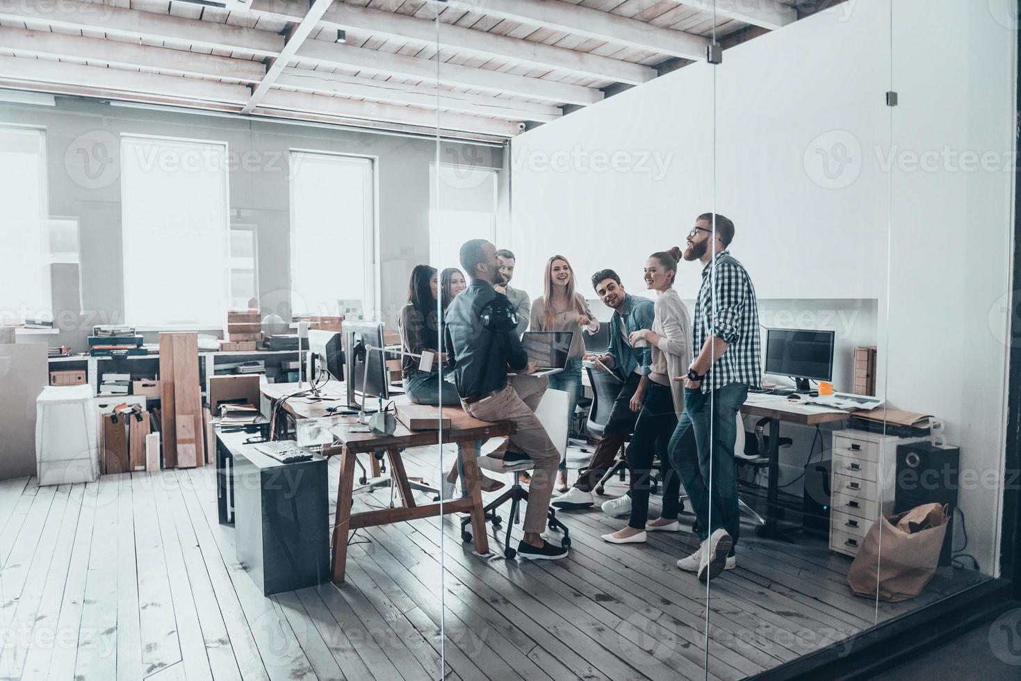 Team at work. Full length of young creative people in smart casual wear having a brainstorm meeting while standing behind the glass wall in the creative office photo