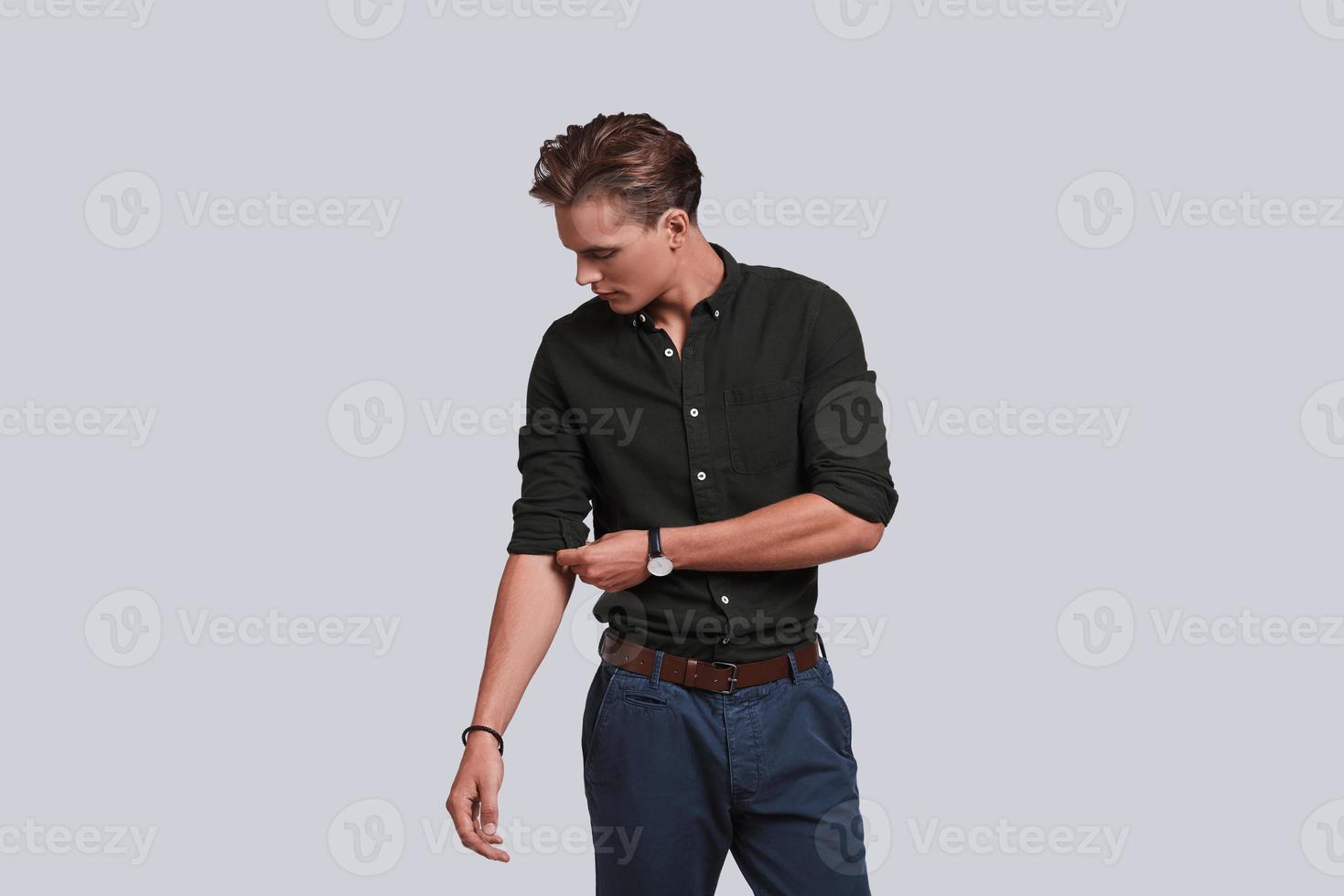 Used to look perfect. Good looking young man adjusting the sleeve of his shirt while standing against grey background photo