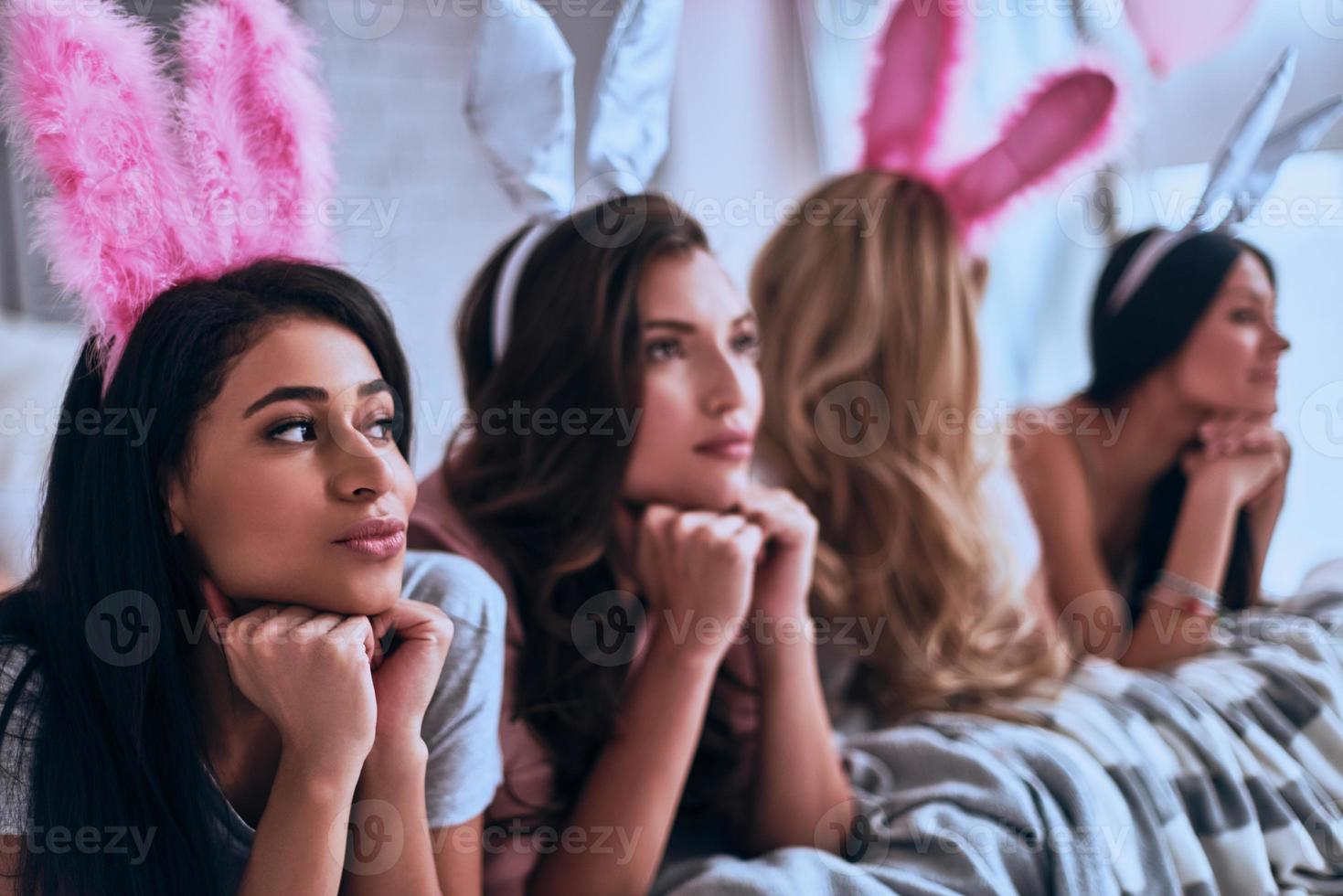Feeling uncertain. Four beautiful young women in bunny ears looking away while lying on the bed photo