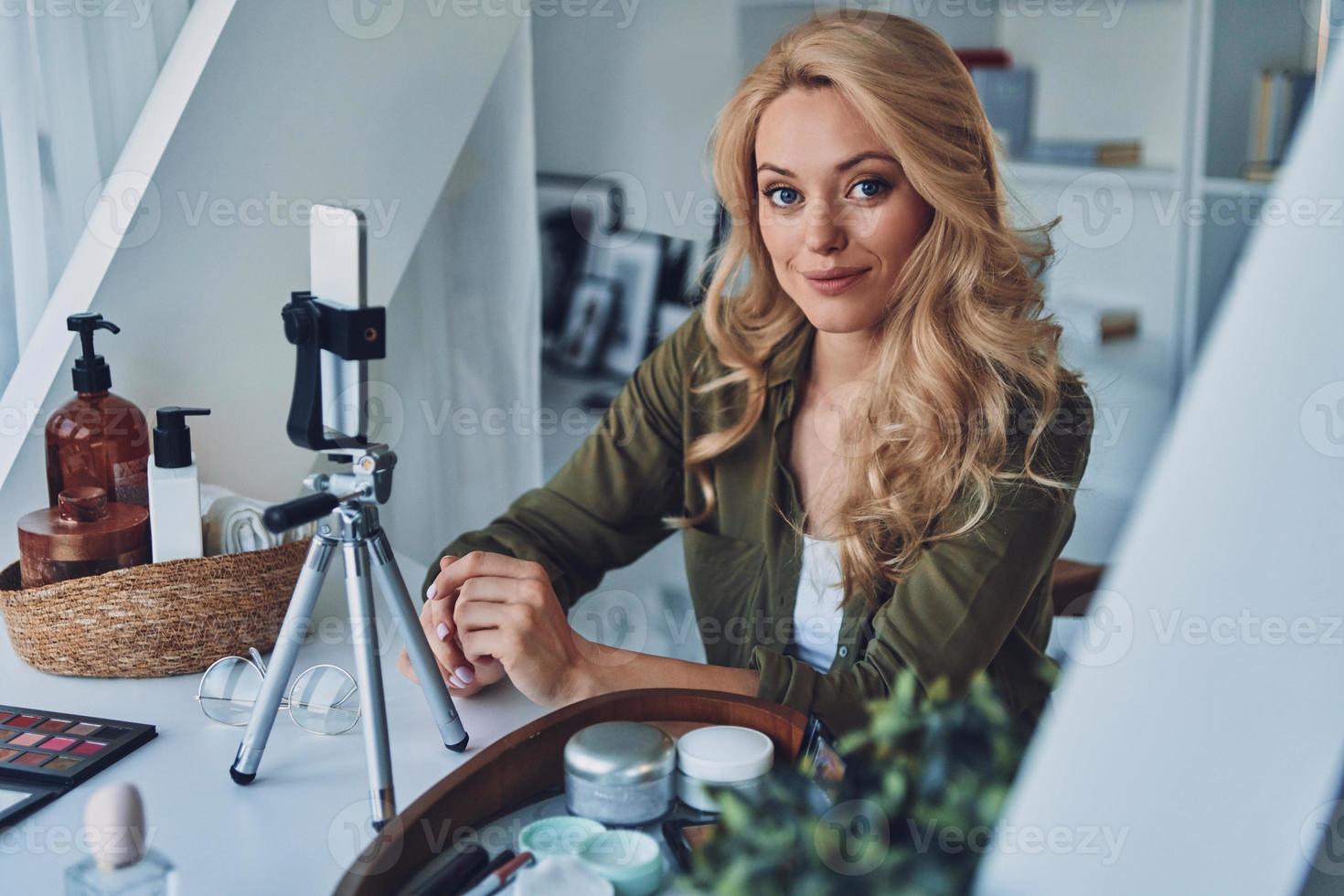 Beautiful young smiling woman vlogging about beauty products and looking at camera photo