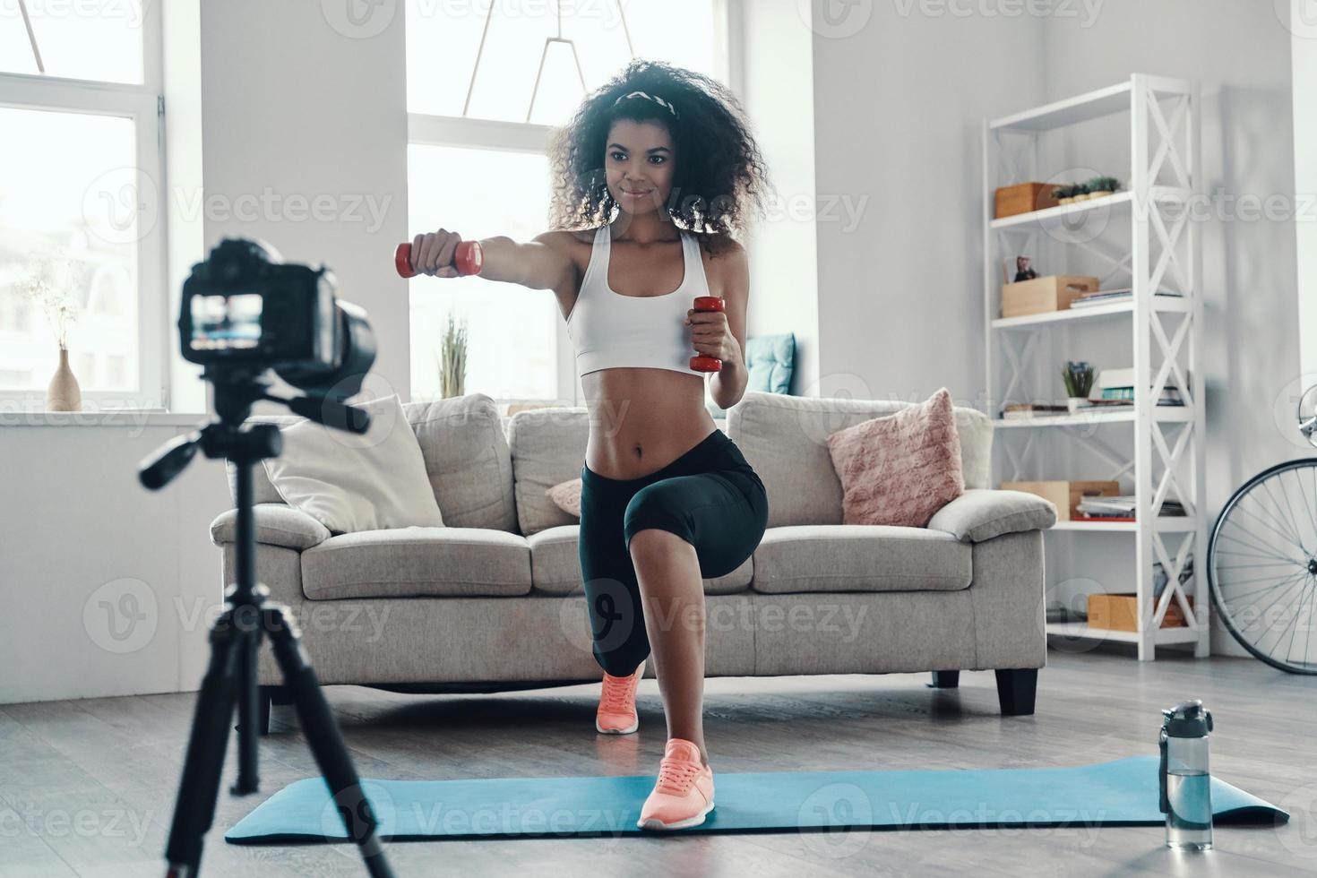 Attractive young African woman exercising using hand weight and smiling while making social media video photo