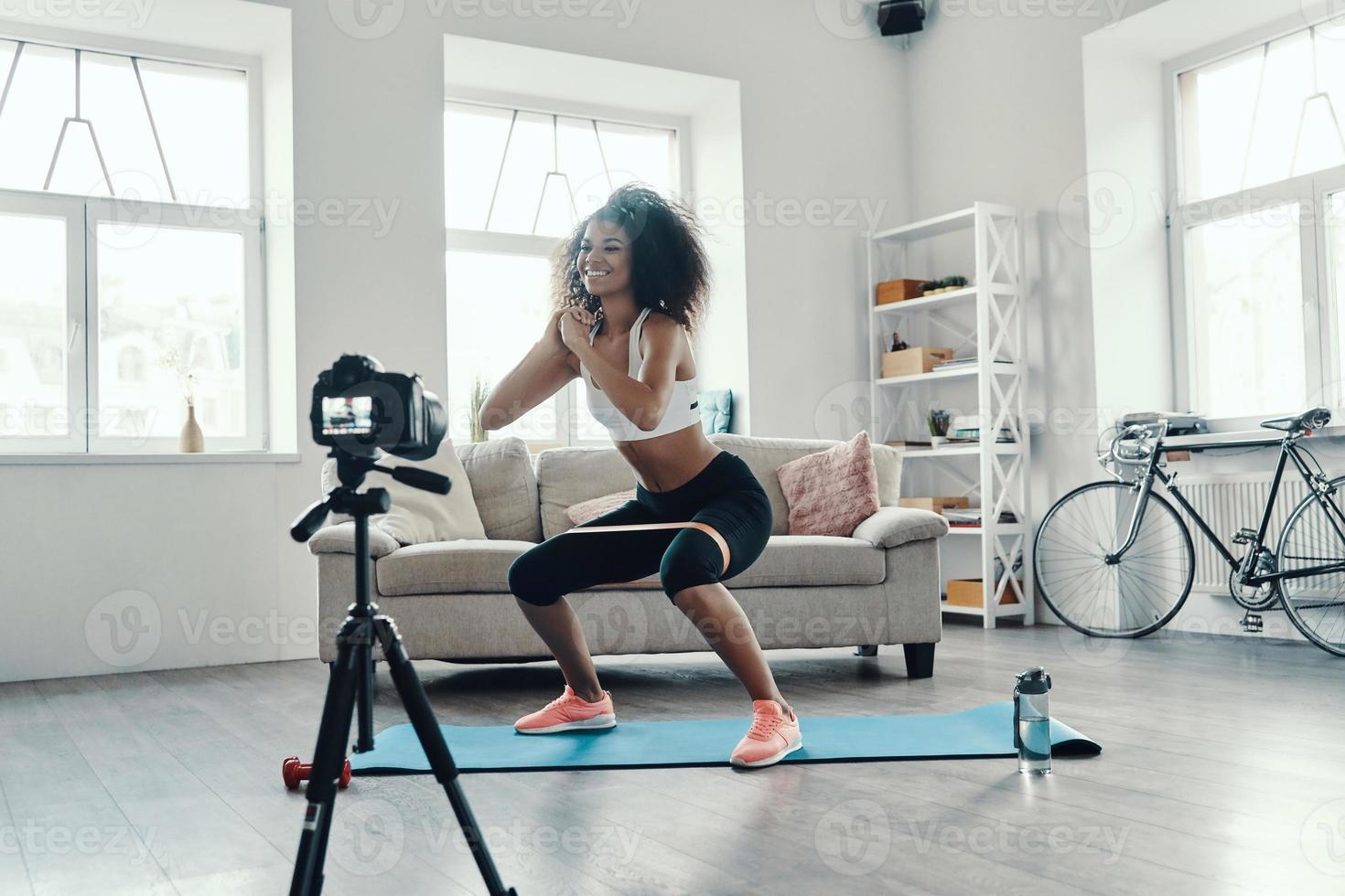 Attractive young African woman crouching using strap while making social media video photo