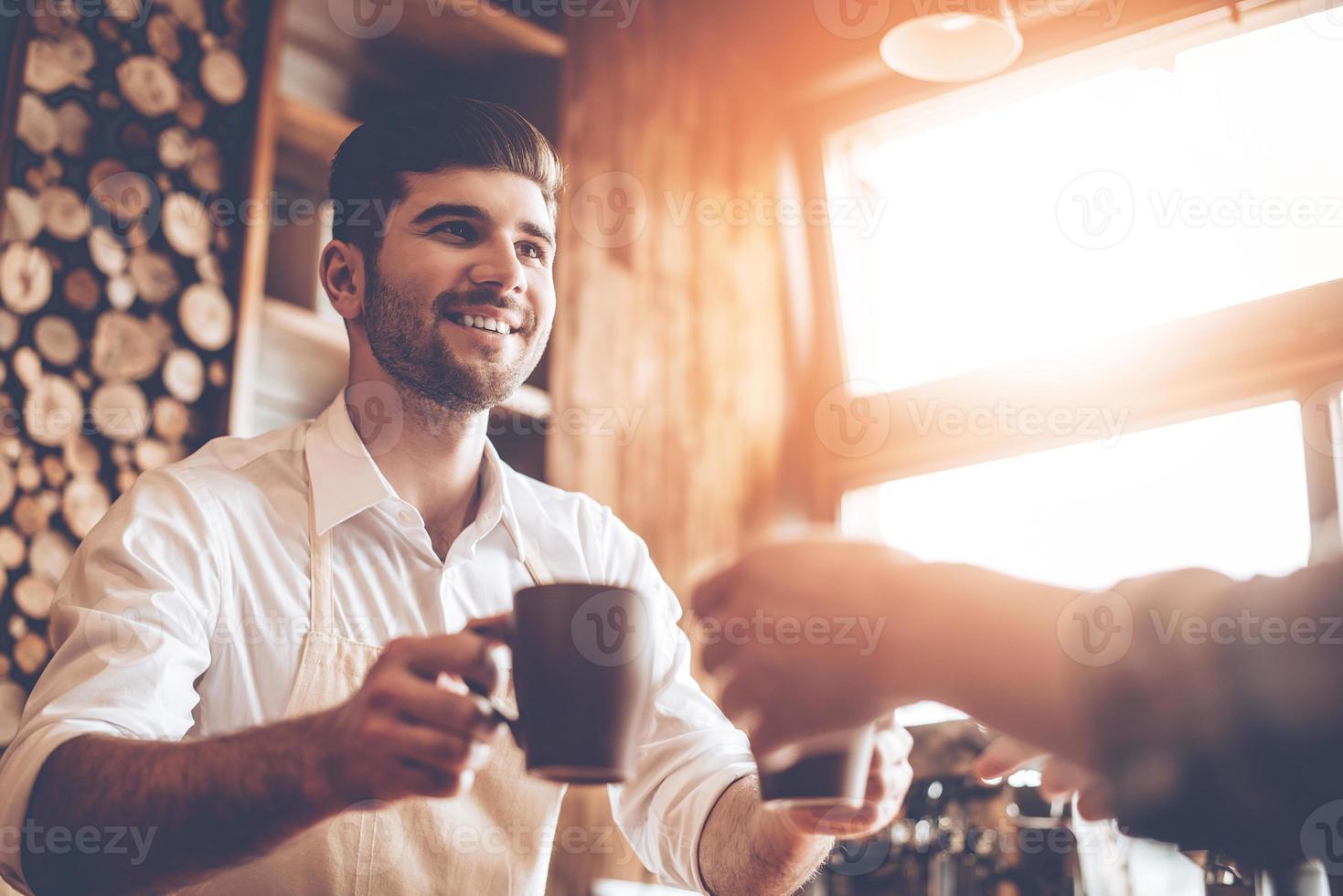 Here is your coffee Close-up part of young handsome man in apron giving two coffee cups to his customer while standing at cafe photo