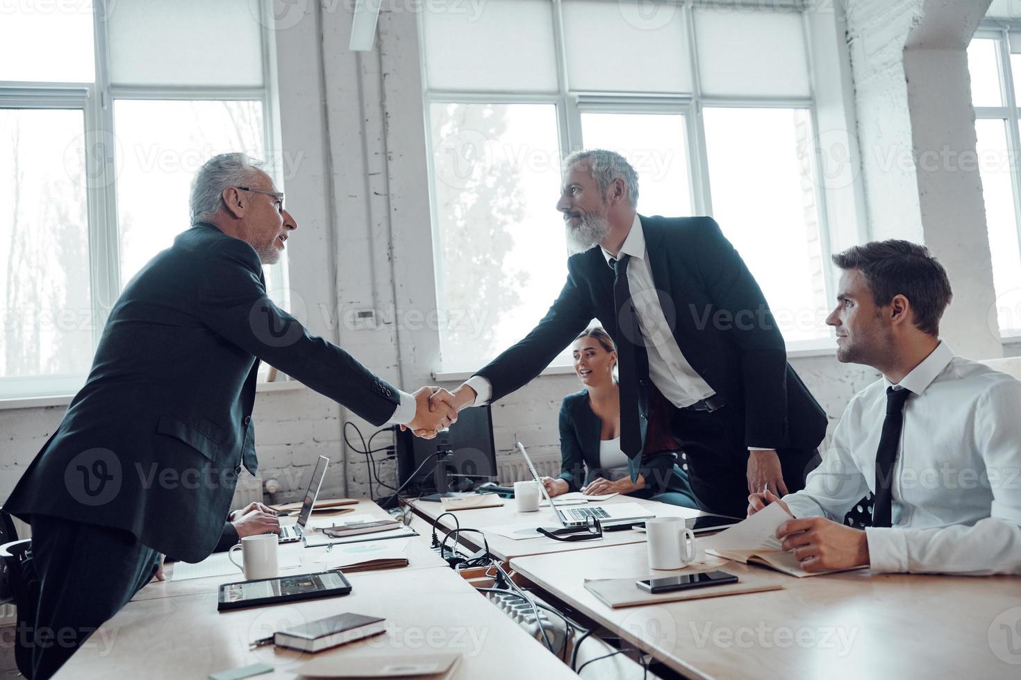 hombres de negocios modernos dándose la mano mientras trabajan junto con su equipo en la oficina foto
