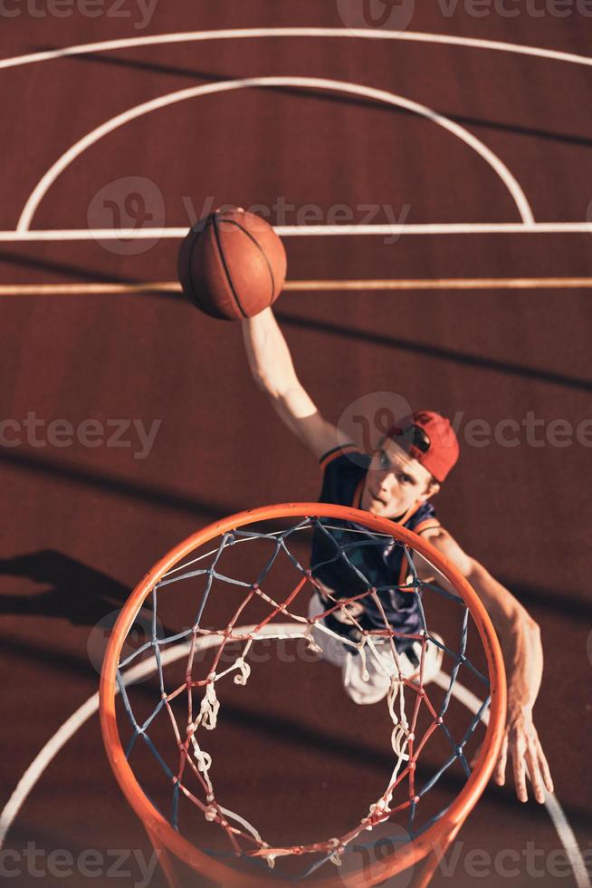 Best basketball player. Top view of young man in sports clothing scoring a slam dunk while playing basketball outdoors photo