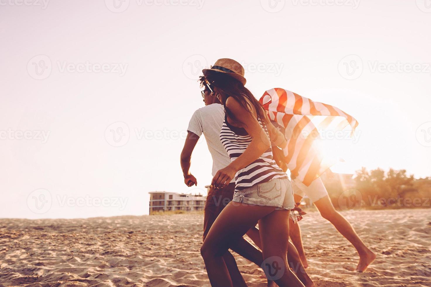 Meeting sunset. Cheerful young people carrying American flag while running along the beach together photo