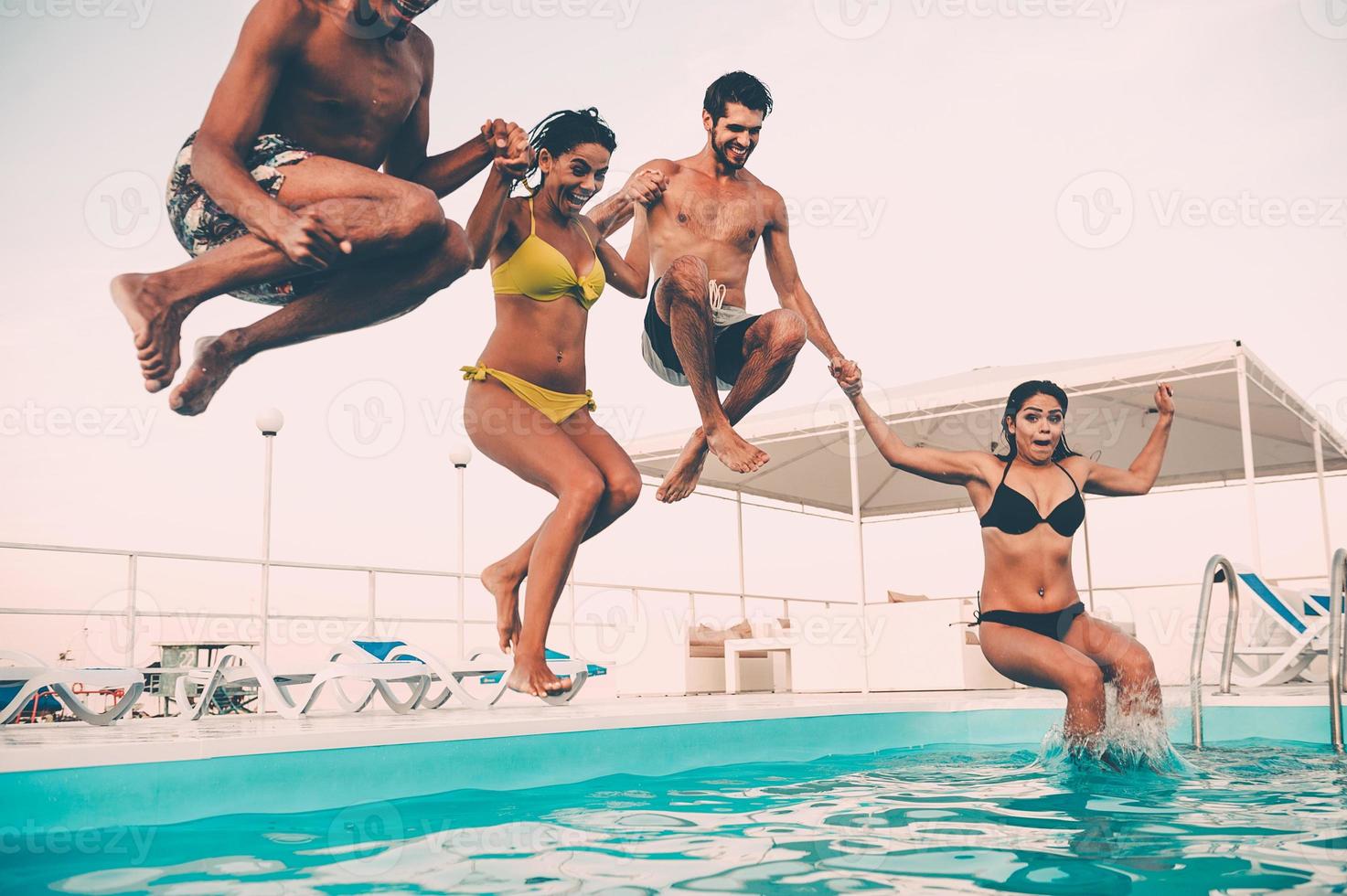 Enjoying pool party together. Group of beautiful young people looking happy while jumping into the swimming pool together photo