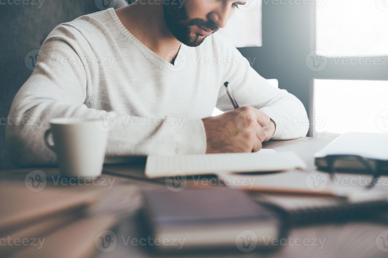 Making some important notes. Close-up of confident young man writing something in notebook while sitting at his working place in office photo
