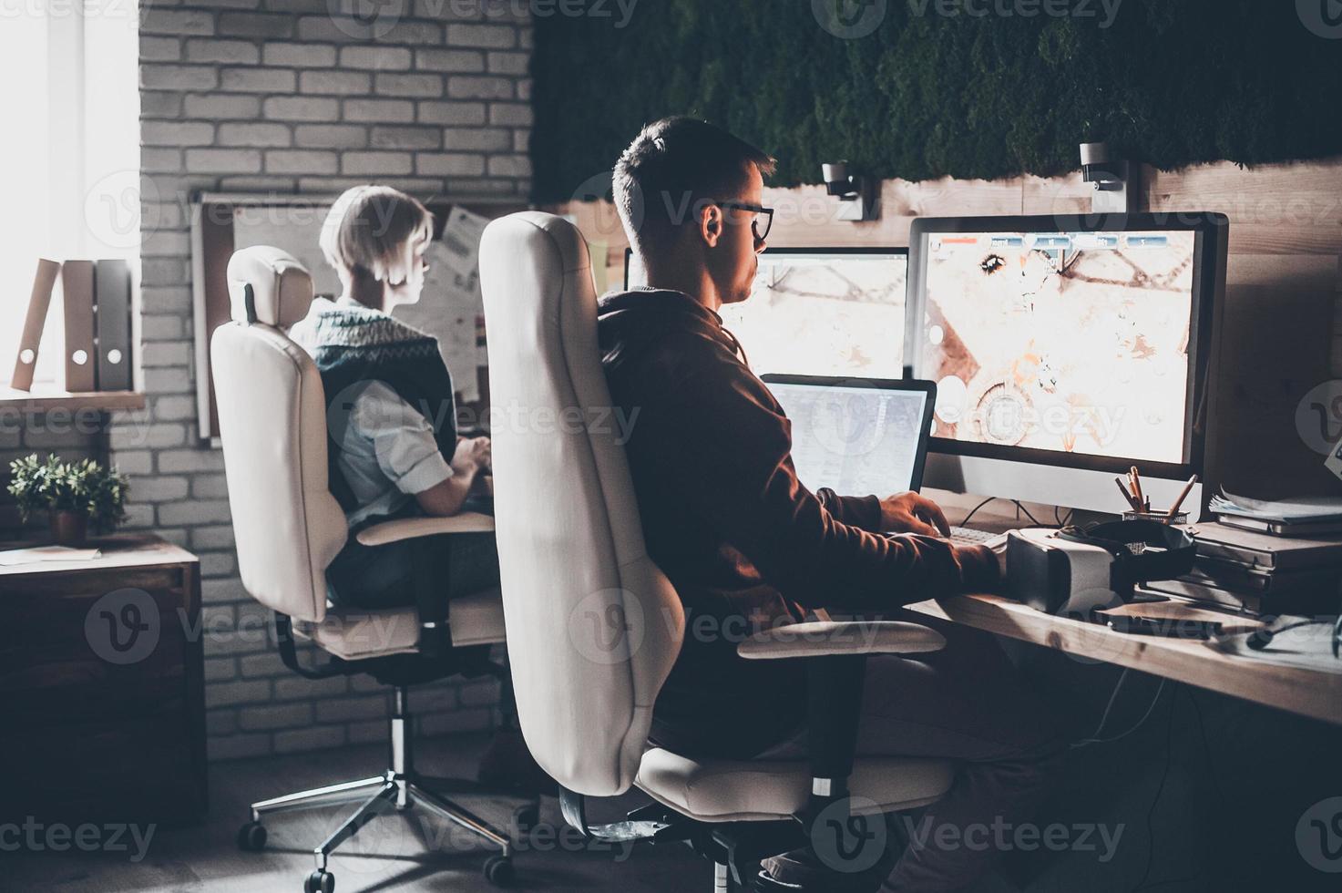 Working with modern technologies. Rear view of young business team working and looking at monitor while sitting at the desk in creative office photo