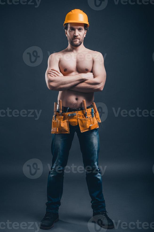 Construction worker. Full Length of young confident man keeping arms crossed and looking at camera while standing against black background photo