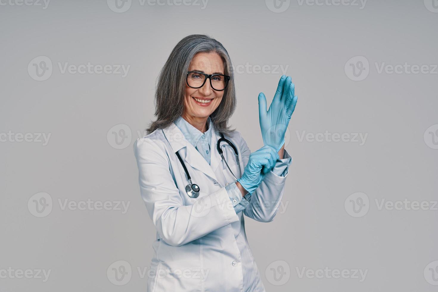 hermosa doctora madura poniéndose guantes quirúrgicos y sonriendo foto