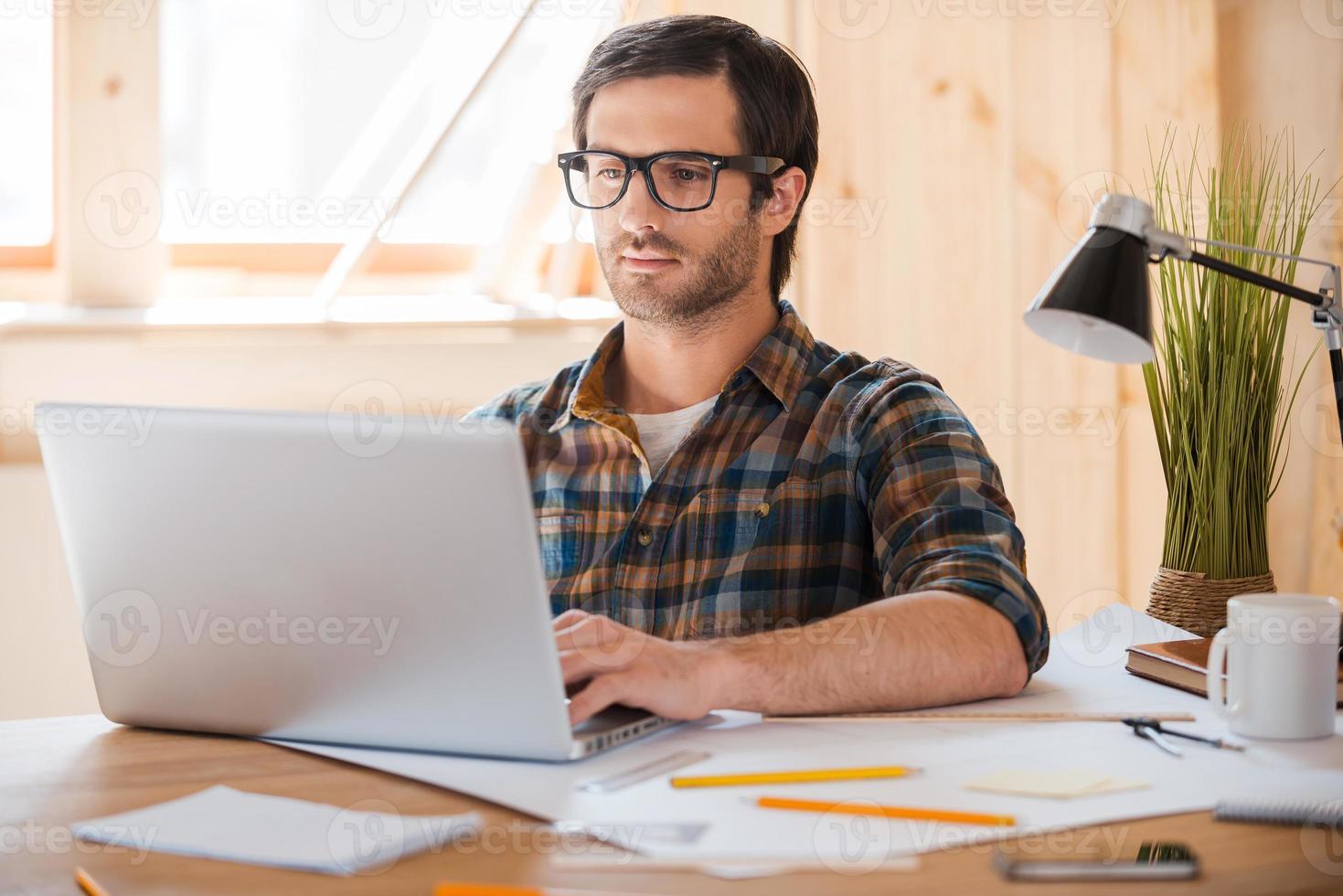 Modern technology for creative work. Confident young man working on laptop while sitting at his working place photo