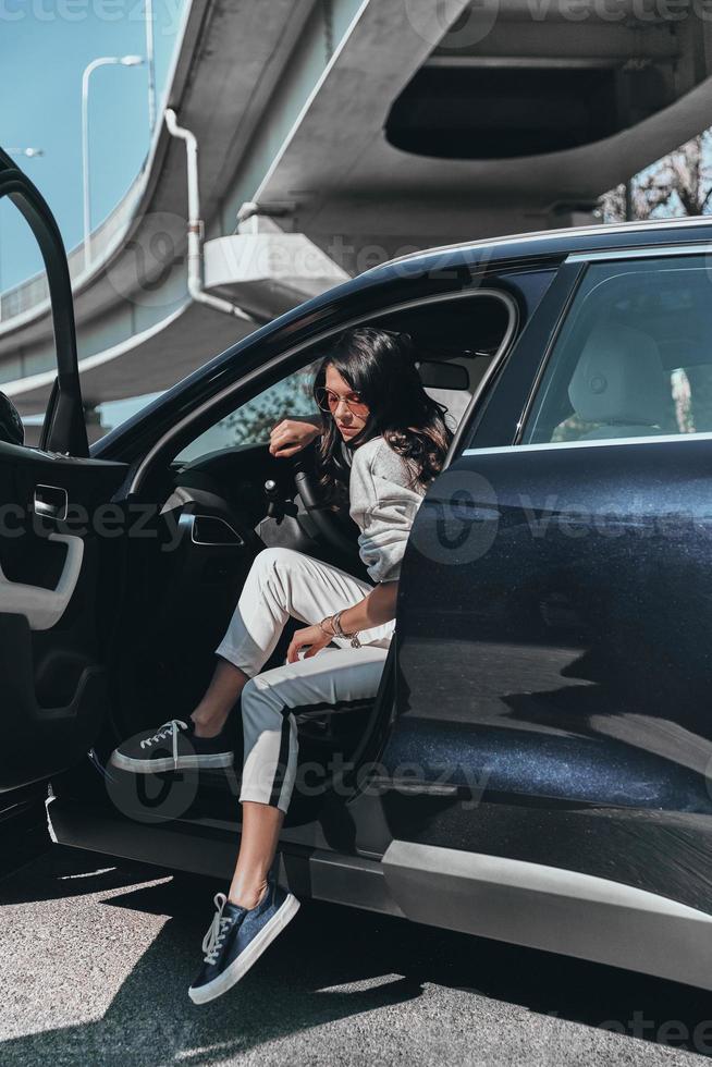 belleza en coche. Atractiva mujer joven y elegante con anteojos saliendo de su auto foto