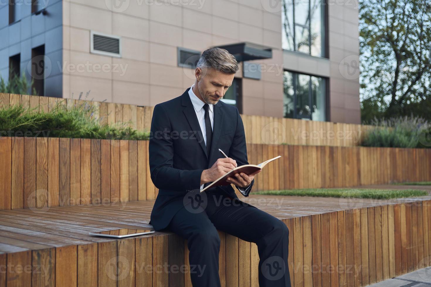 Confident mature businessman using digital tablet while sitting outdoors near office building photo