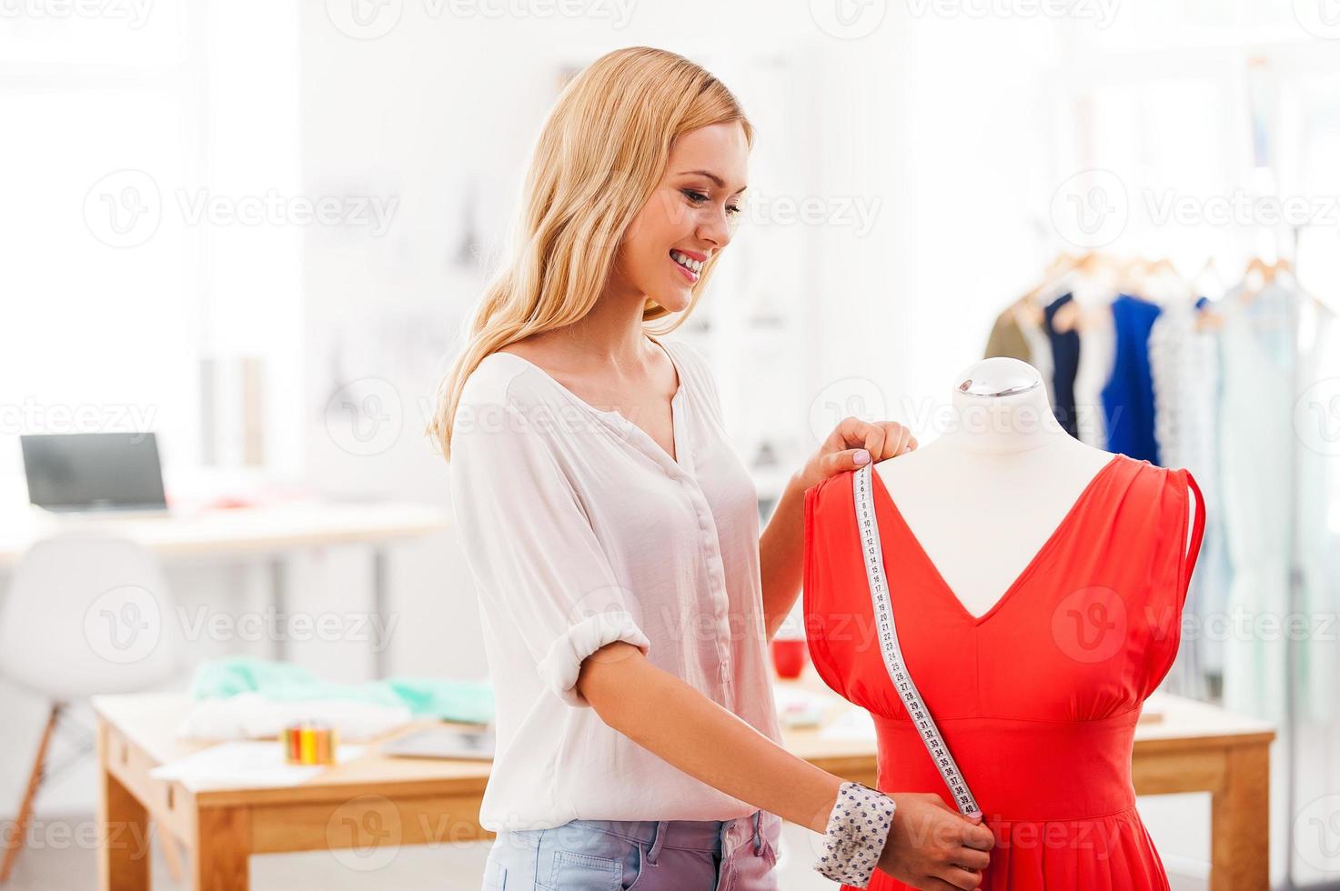 The perfect length Happy young woman taking measurements from dress while standing in her fashion workshop photo