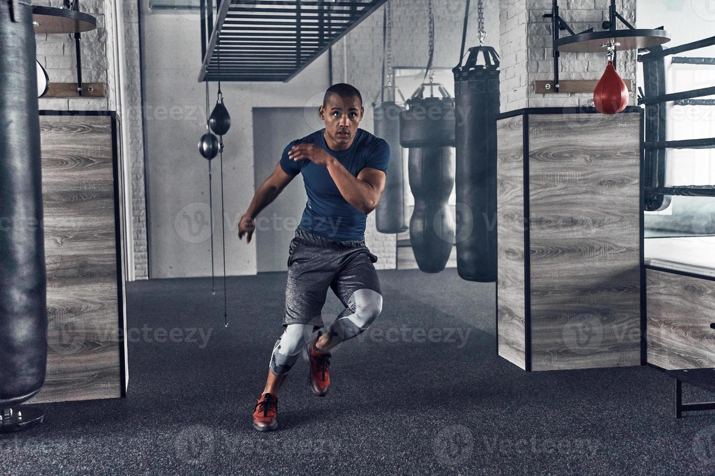 Just keep moving. Full length of handsome young African man in sport clothing running while exercising in the gym photo