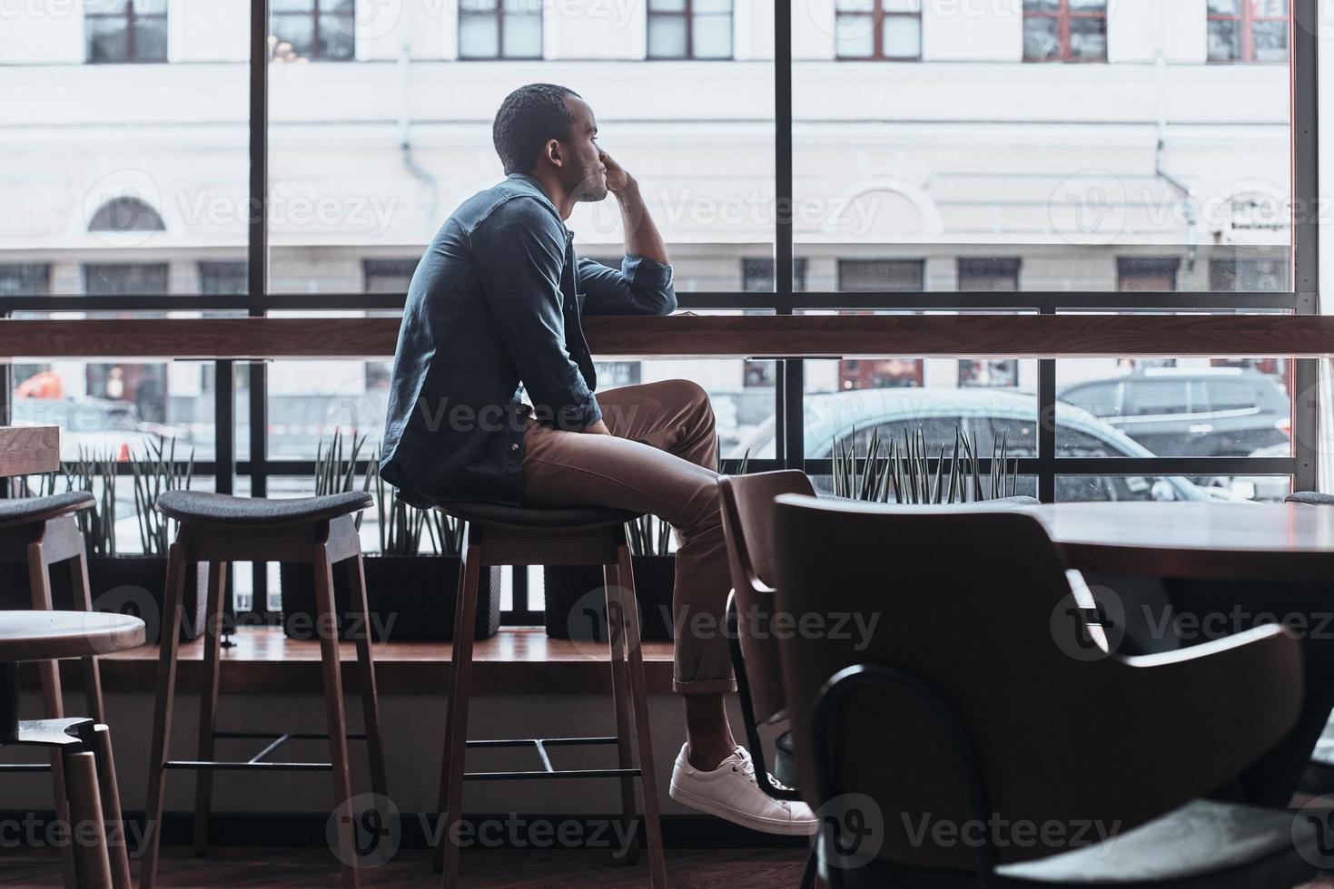 Enjoying nice day. Thoughtful young man looking outside while sitting in the cafeteria photo