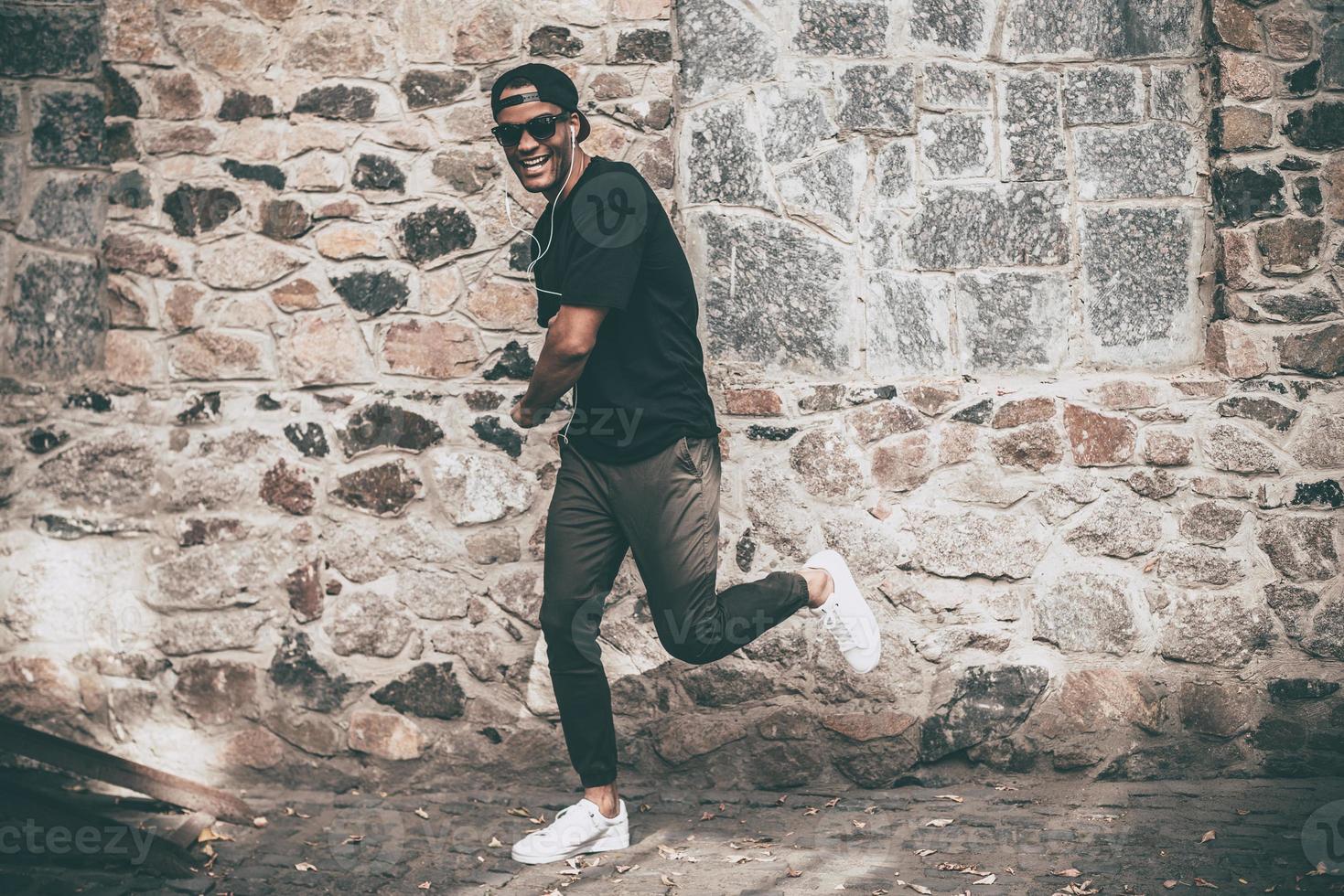 Like a real star Full length of handsome young African man in headphones singing and dancing in front of the stoned wall outdoors photo