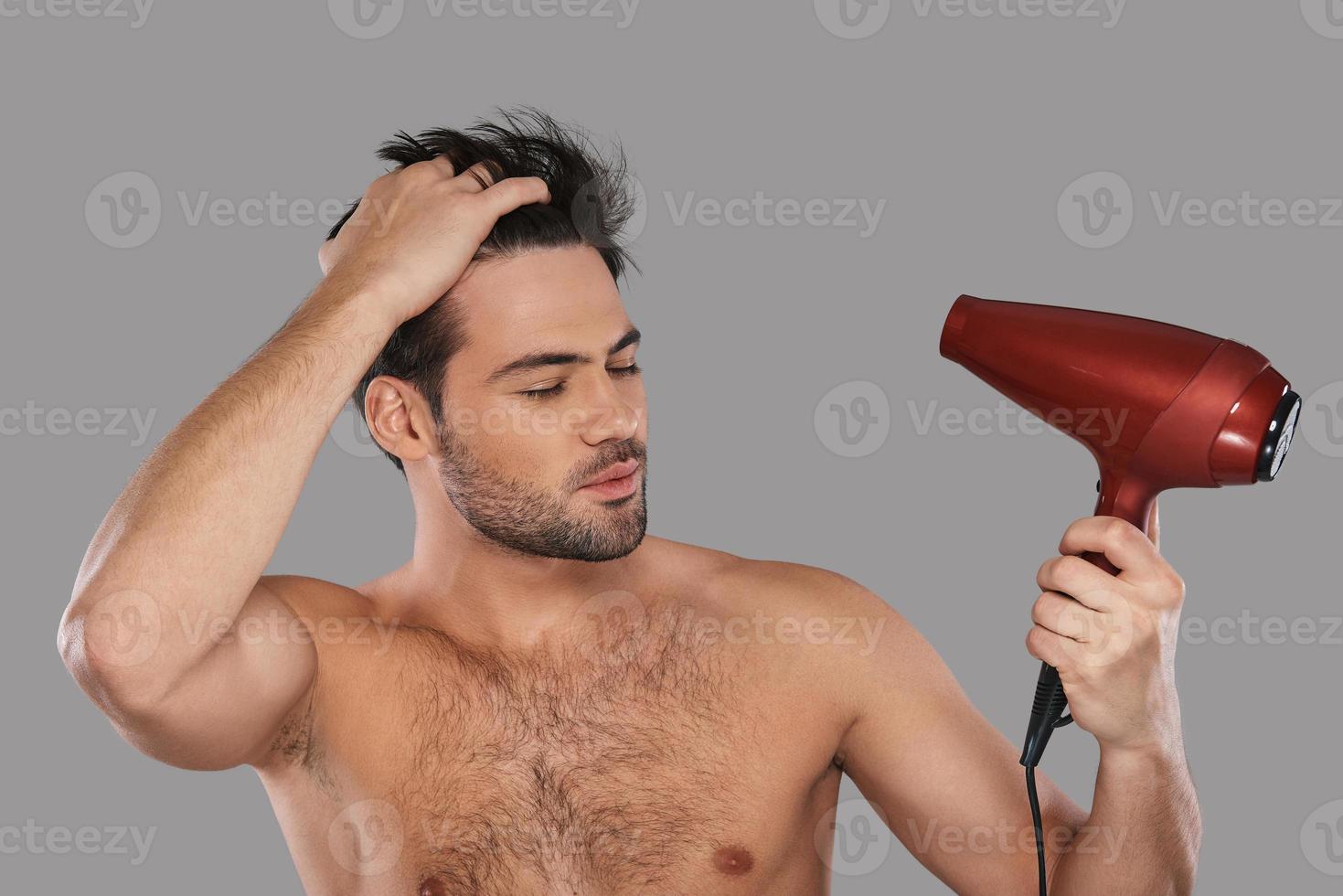 solía lucir perfecto. un joven guapo secándose el pelo y manteniendo los ojos cerrados mientras se enfrenta a un fondo gris foto