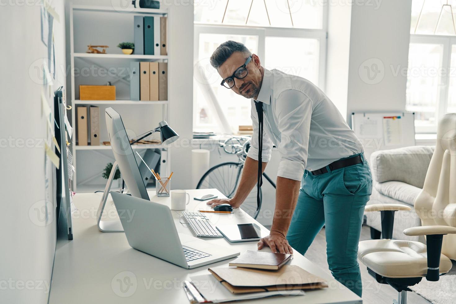 Modern businessman. Handsome young man looking away and smiling while standing in the office photo