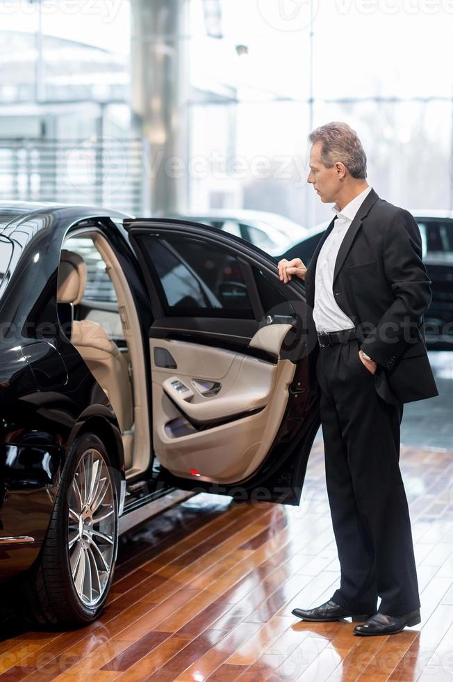 Examining car at dealership. Full length of confident mature man in formalwear opening the car door at the dealership photo