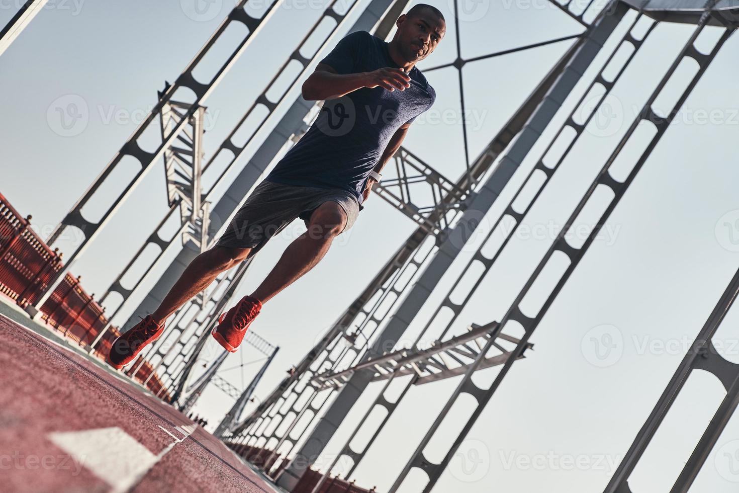 You can do it Full length of young African man in sports clothing exercising while jogging on the bridge outdoors photo